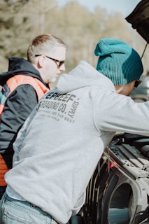 a couple of men standing next to a parked car
