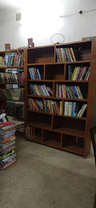 Spacious room interior with wooden flooring, a bed, and a small bookshelf filled with books.