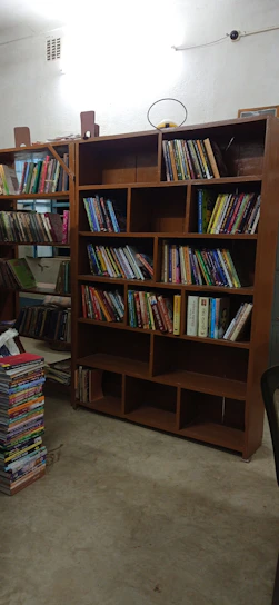 Spacious room interior with wooden flooring, a bed, and a small bookshelf filled with books.
