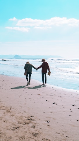 Two people walking hand in hand along a scenic beach.