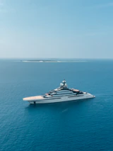 A yacht sailing smoothly on calm blue waters with a bright sky overhead.