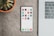 A sleek smartphone displaying various banking app icons is placed on a grey surface. To the left, there is a potted succulent plant, and on the right, part of a laptop keyboard is visible.