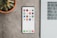 A sleek smartphone displaying various banking app icons is placed on a grey surface. To the left, there is a potted succulent plant, and on the right, part of a laptop keyboard is visible.