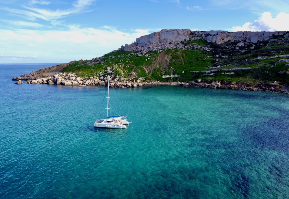 a sailboat in the water near a rocky shore