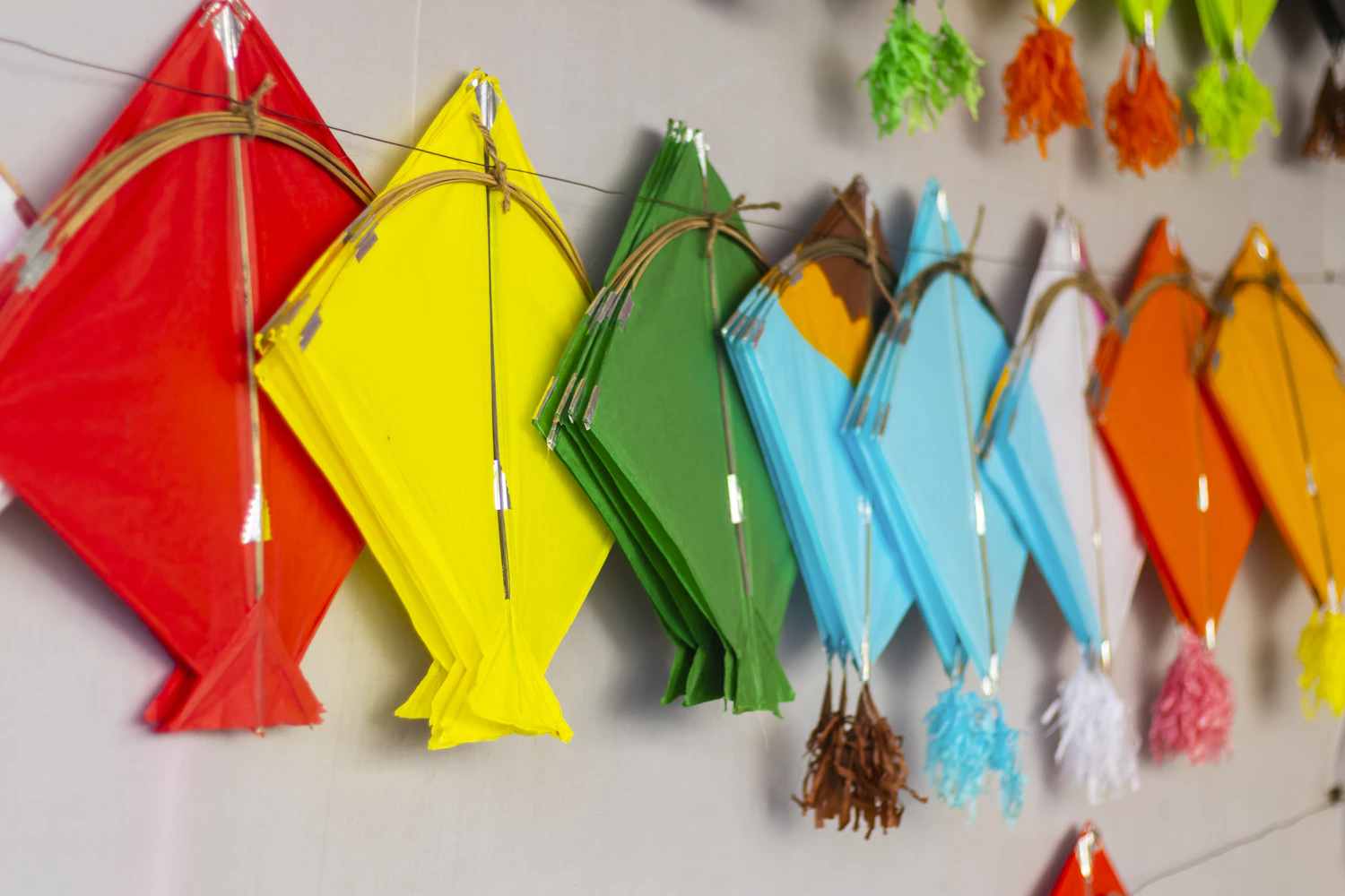 Yellow, green and blue paper kites with tassels hanging on a workshop wall