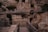 Ancient stone ruins are partially reconstructed with modern metal railings for visitors. Weathered stone walls and arches, surrounded by rough vegetation, create a sense of historical depth and mystery.