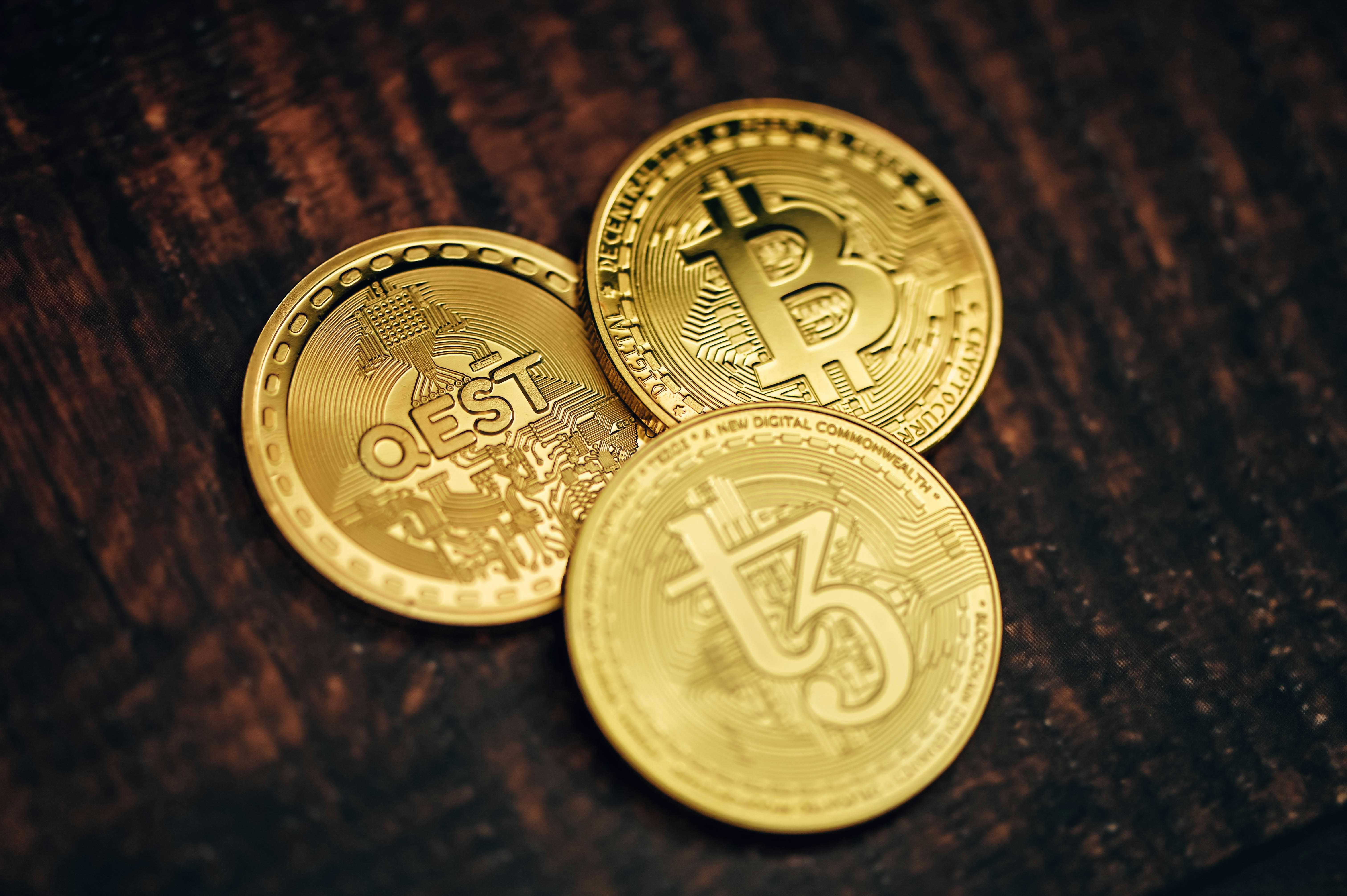 QEST coin, Bitcoin, and Tezos coin placed on a wooden background