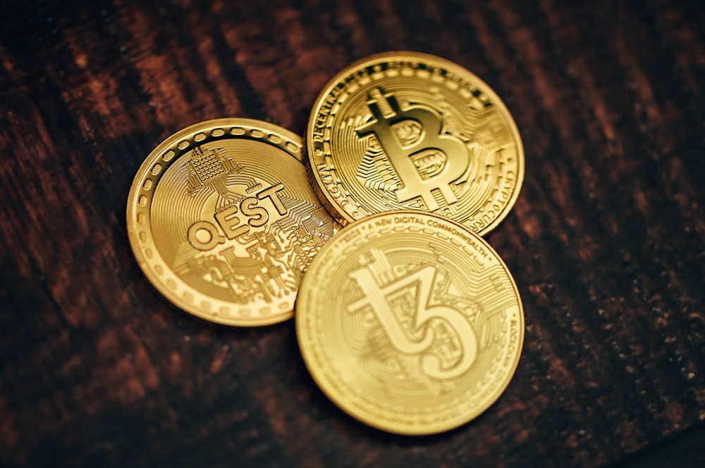 Tres bitcoins de oro sentados encima de una mesa de madera