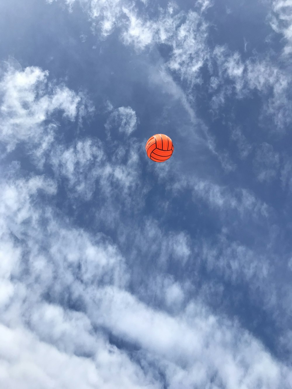 an orange kite flying through a cloudy blue sky