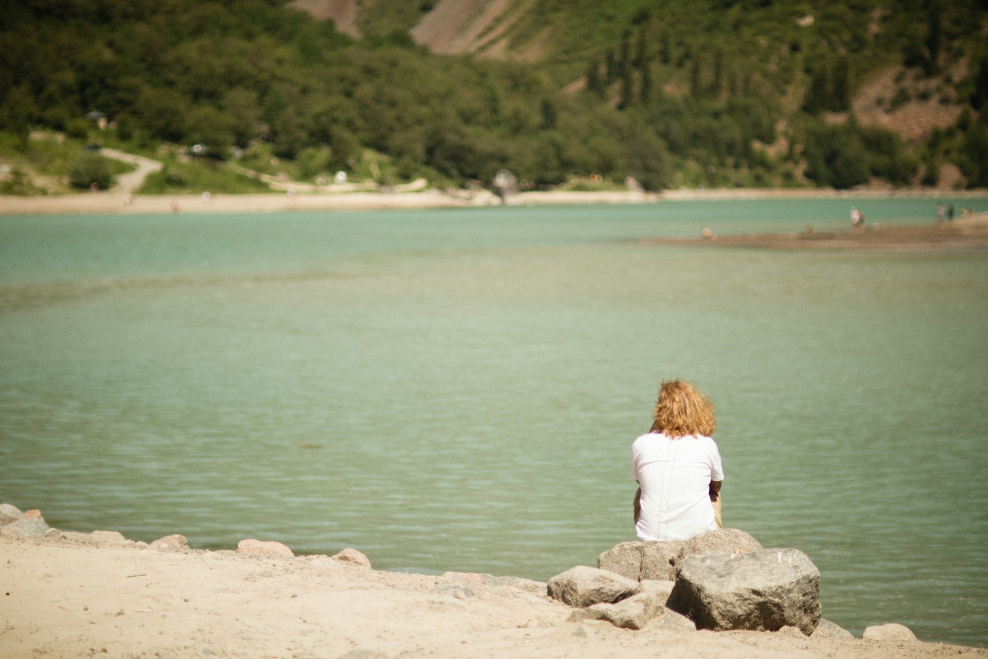 a woman sitting on a rock looking at the water