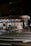 A small supermarket is illuminated at night with light shining from the store’s interior. The parking area is empty, and a shopping cart can be seen outside. The supermarket has a red sign with white lettering.