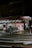 A small supermarket is illuminated at night with light shining from the store’s interior. The parking area is empty, and a shopping cart can be seen outside. The supermarket has a red sign with white lettering.