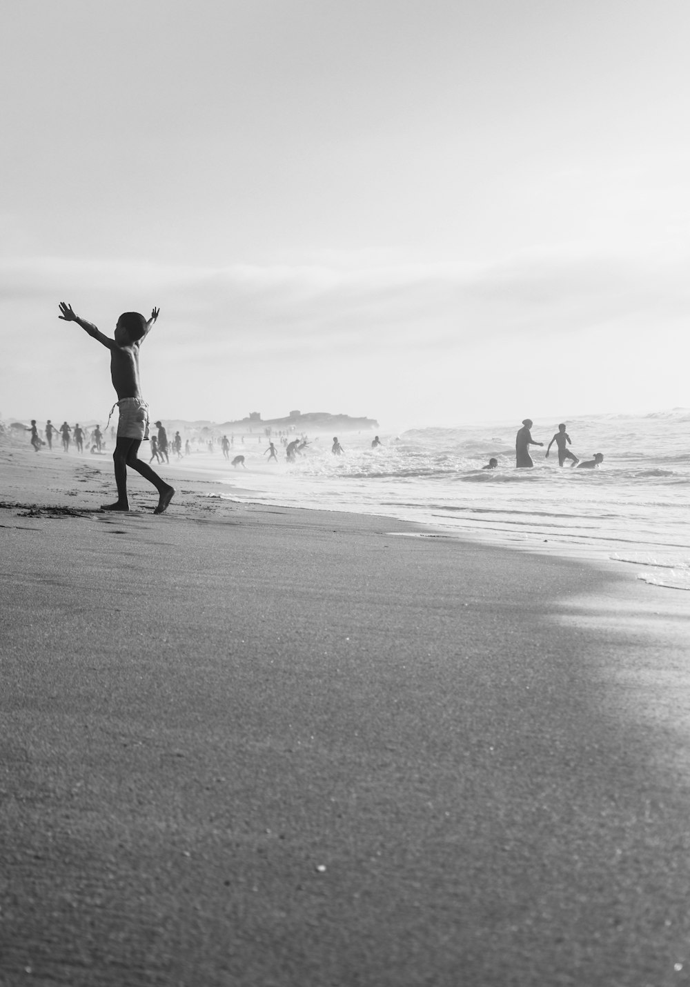 a young boy standing on top of a beach next to the ocean