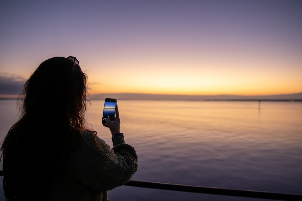 a woman taking a picture of a sunset with her cell phone