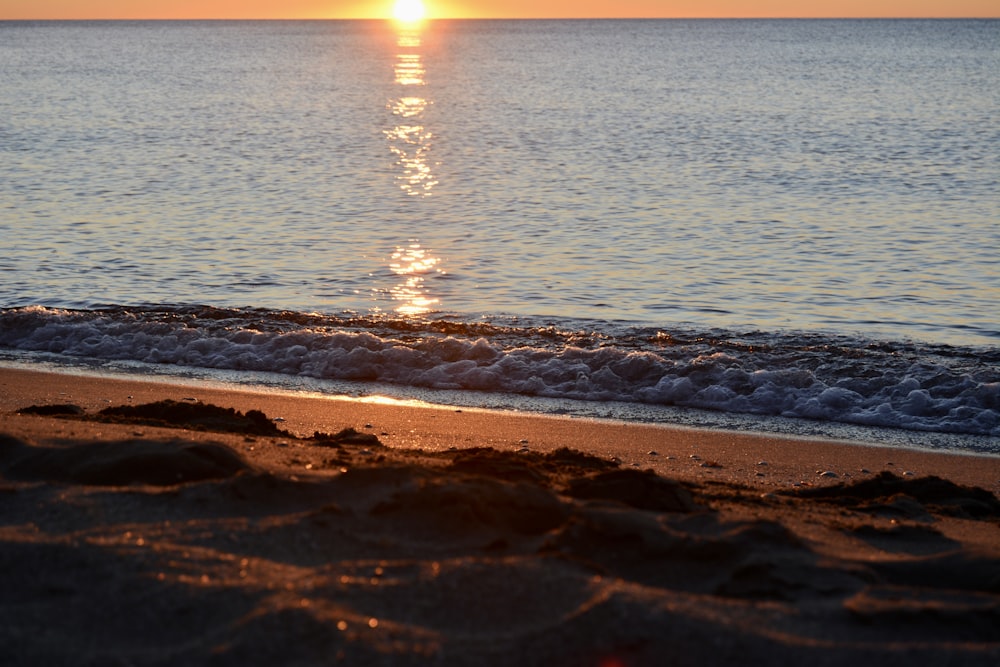 the sun is setting over the water at the beach