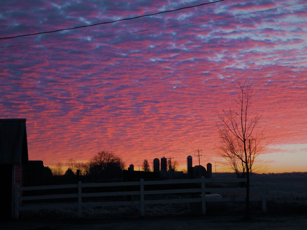 a pink and purple sky at sunset over a farm