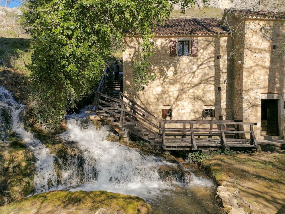 a house next to a waterfall with a wooden bridge