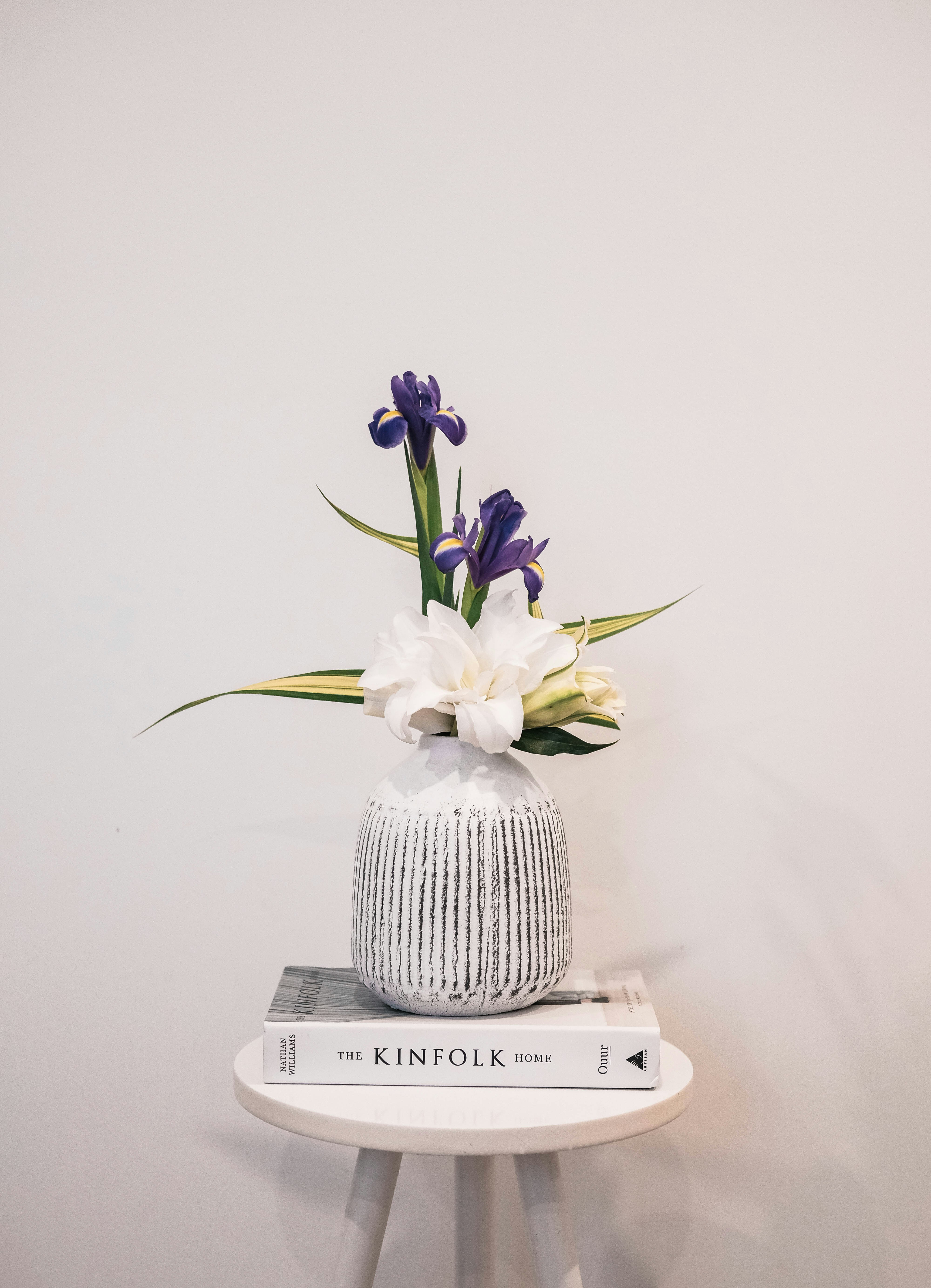 a white vase with purple and white flowers on top of a stack of books