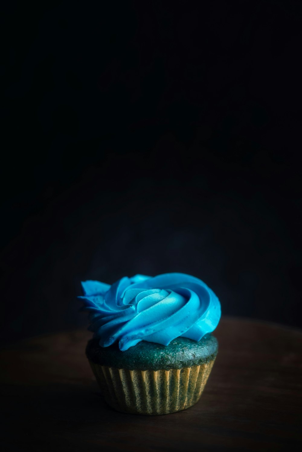 a cupcake with blue frosting on a wooden table