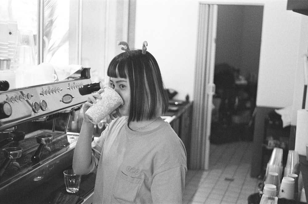 a woman standing in a kitchen drinking from a cup