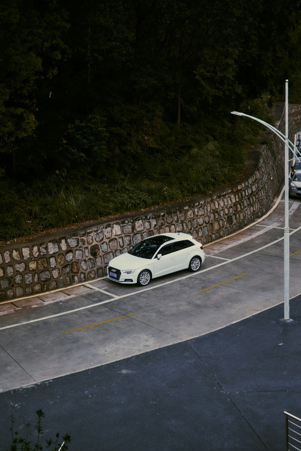 a white car driving down a street next to a stone wall