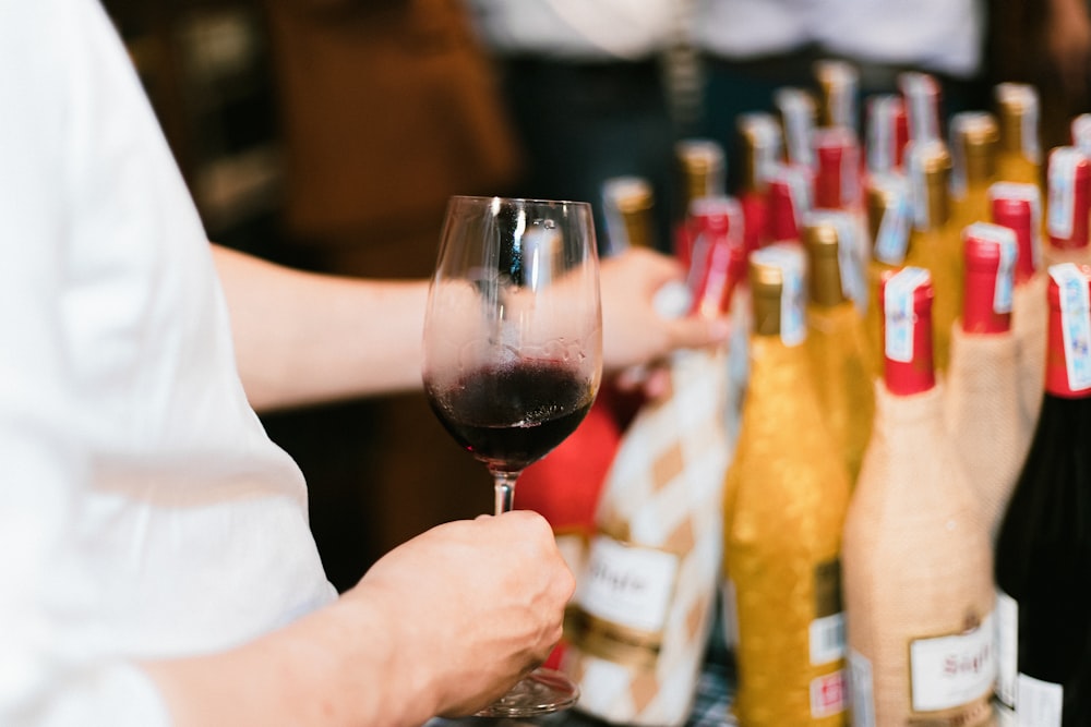 a person holding a wine glass in front of a row of bottles