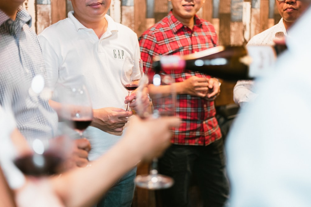 a group of men standing next to each other holding wine glasses