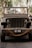 A vintage military jeep is adorned with a 'just married' sign on the windshield. The vehicle is parked on a paved path, surrounded by greenery. Thick ropes are coiled around the front, and the scene is bathed in soft, natural light.