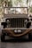 A vintage military jeep is adorned with a 'just married' sign on the windshield. The vehicle is parked on a paved path, surrounded by greenery. Thick ropes are coiled around the front, and the scene is bathed in soft, natural light.