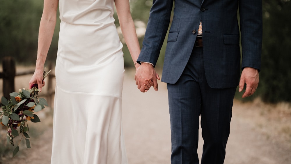 Eine Braut und ein Bräutigam, die Händchen halten und einen Pfad entlang gehen