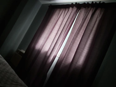 A technician carefully installing blackout curtains in a bright bedroom.