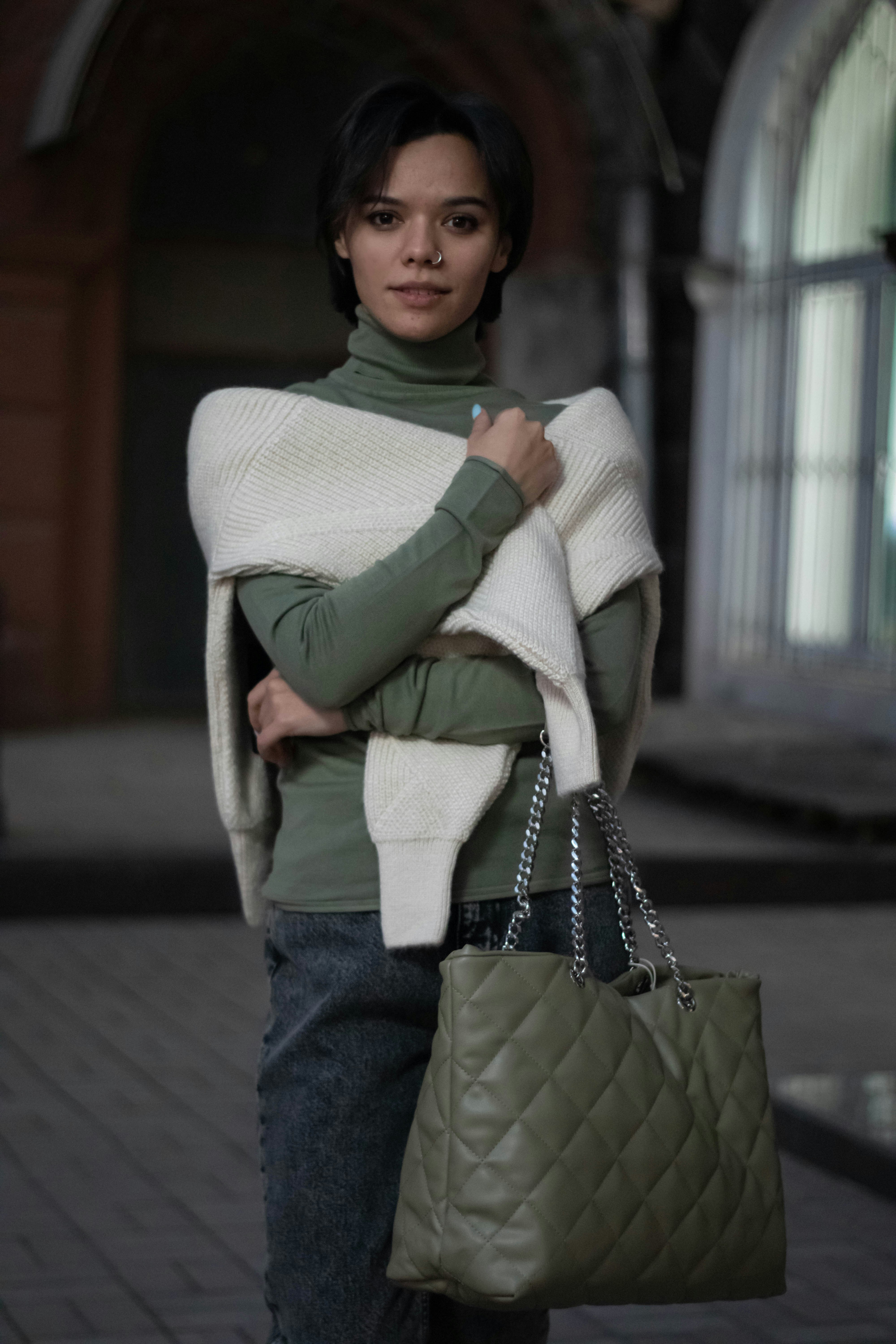 Una mujer que lleva un bolso verde y una manta blanca