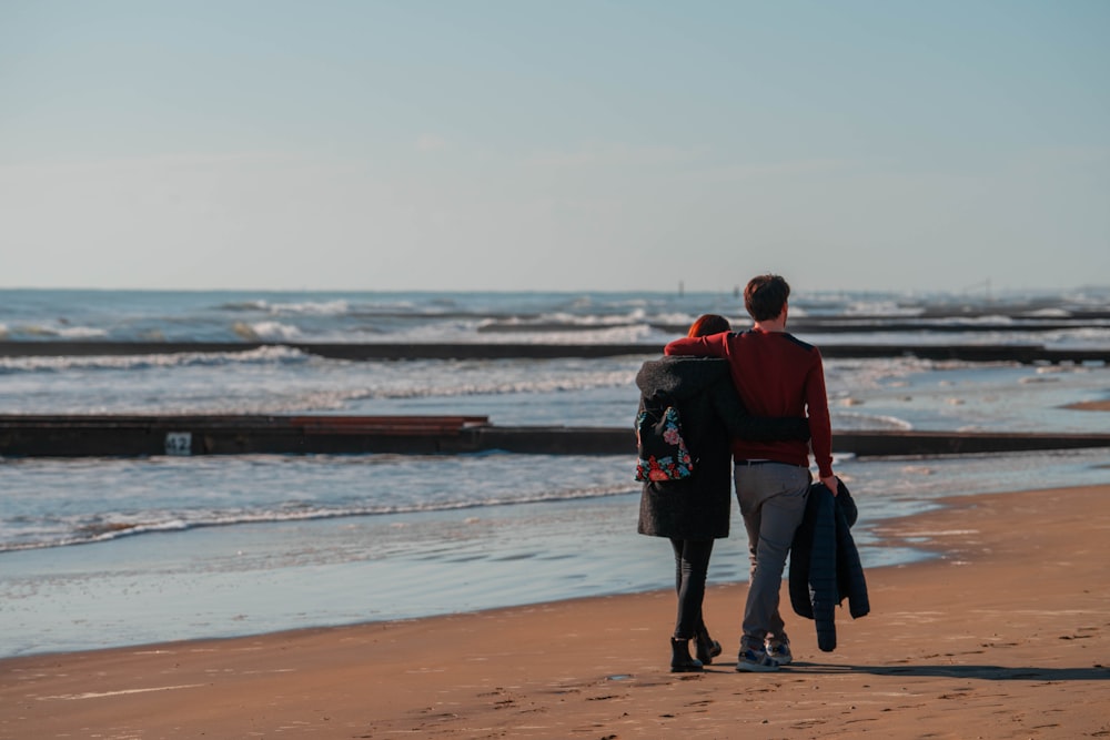 a man and woman walking on a beach next to the ocean