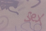A textured wall featuring graffiti with various abstract designs and the word 'sex' written in red.