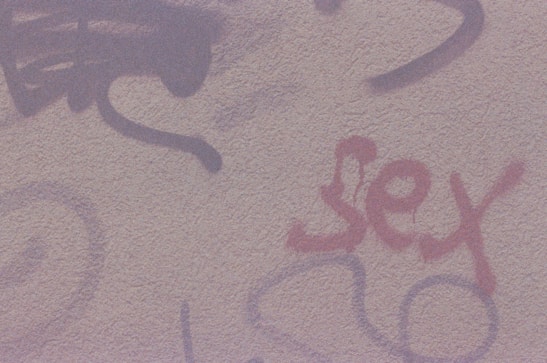 A textured wall featuring graffiti with various abstract designs and the word 'sex' written in red.