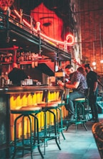 A stylish bar area with colorful cocktails and patrons engaged in conversation.