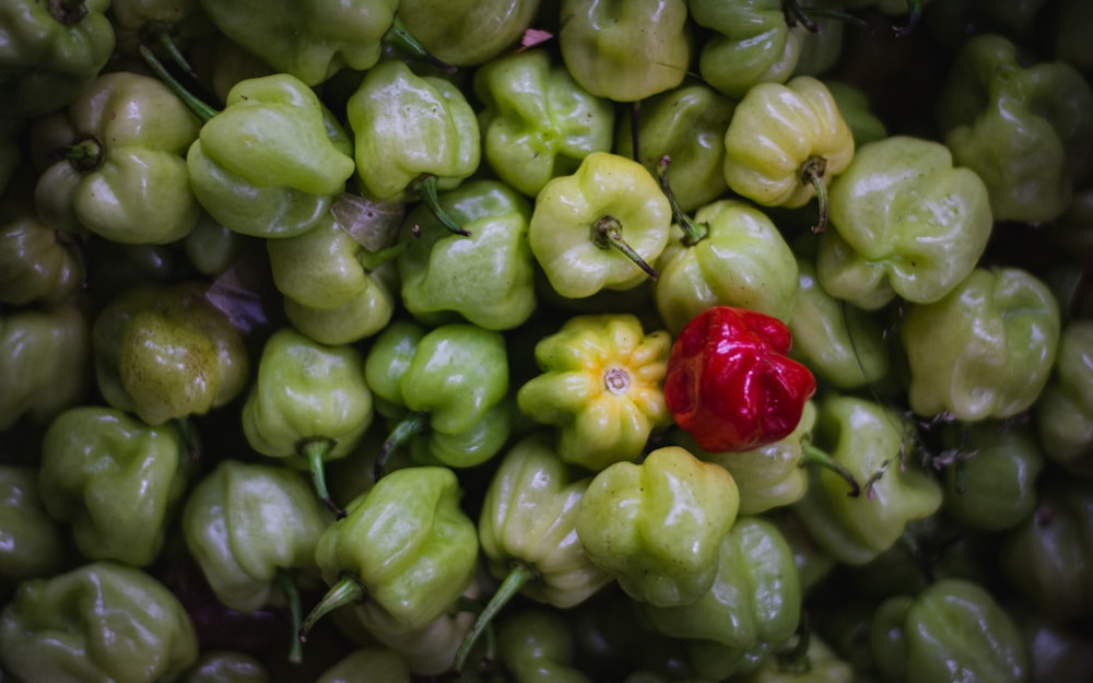 a pile of green peppers with a red pepper in the middle