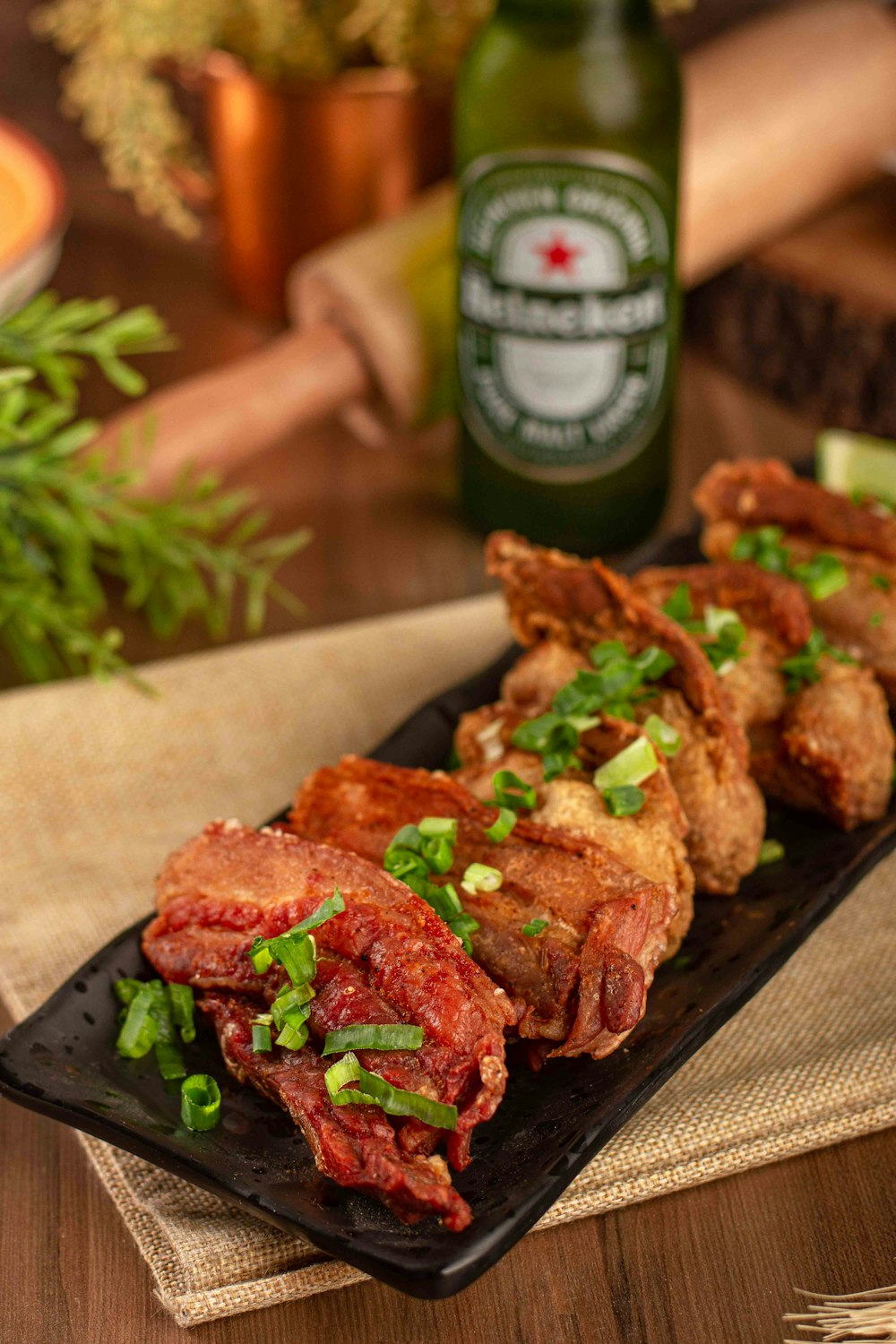 a black plate topped with meat and veggies next to a bottle of beer