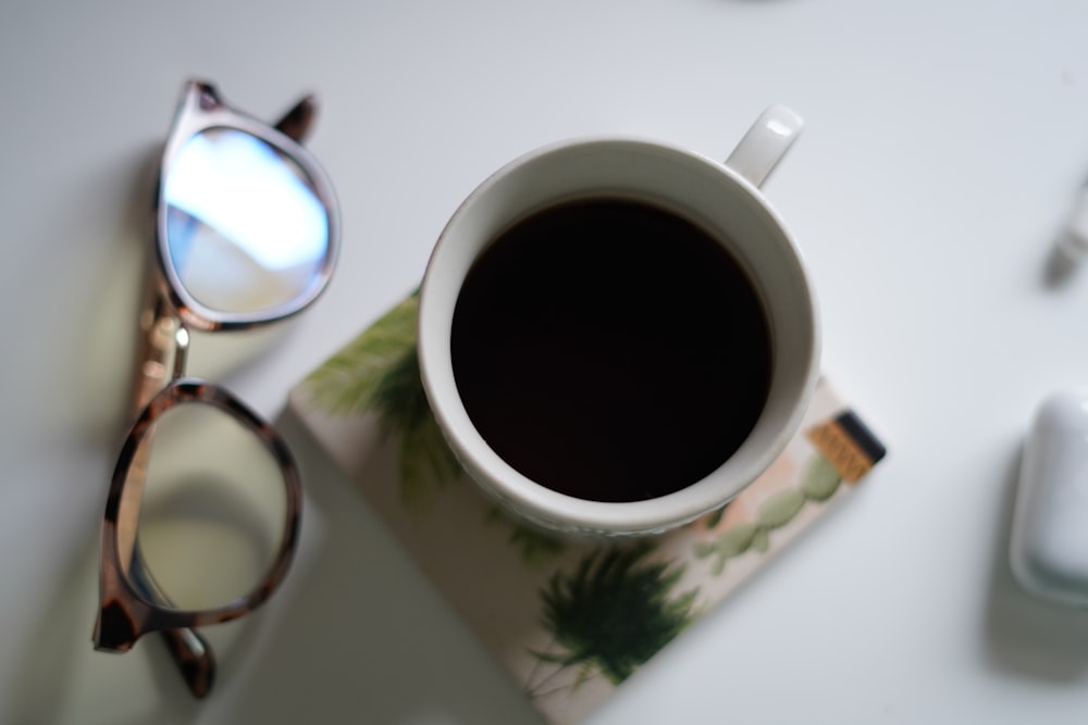 a cup of coffee next to a pair of glasses