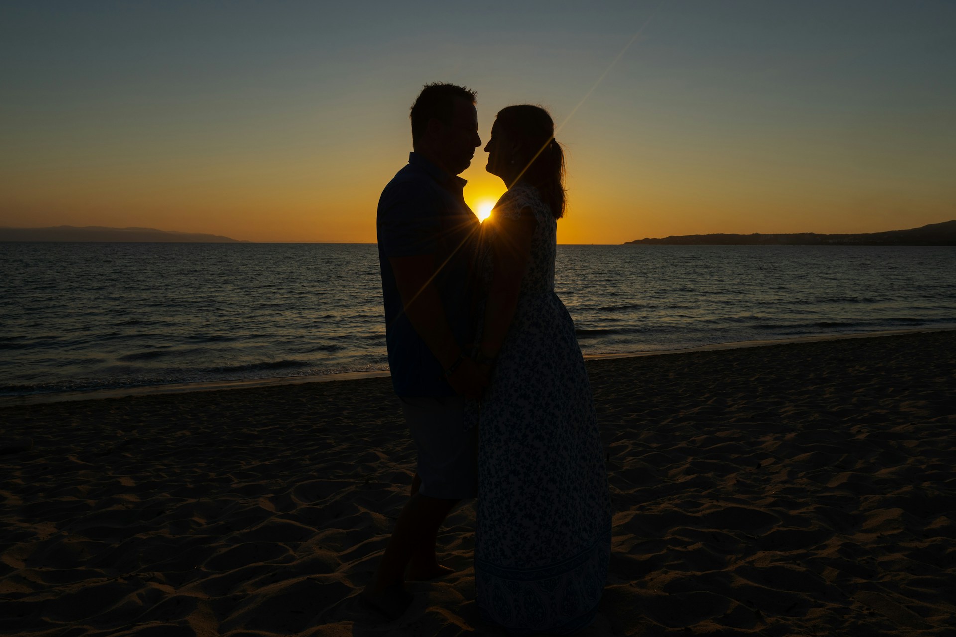 a man and a woman standing on a beach at sunset