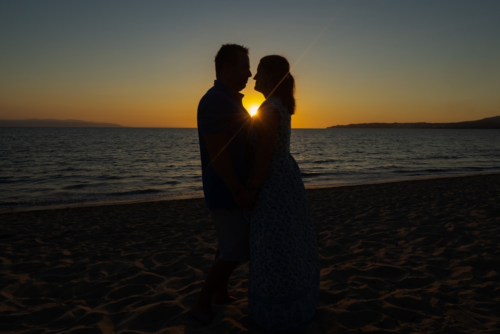 a man and a woman standing on a beach at sunset