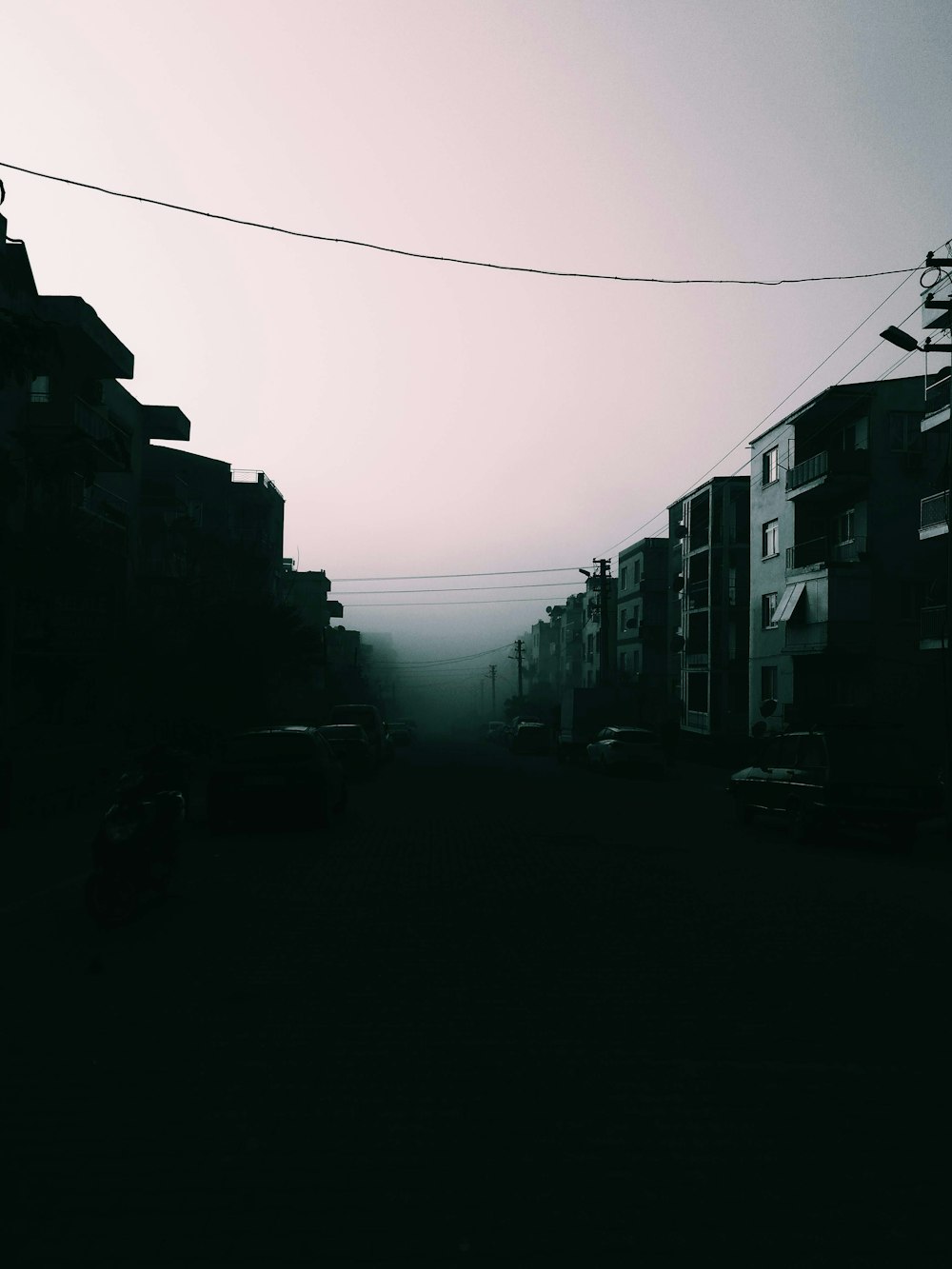a foggy street with cars parked on the side of it
