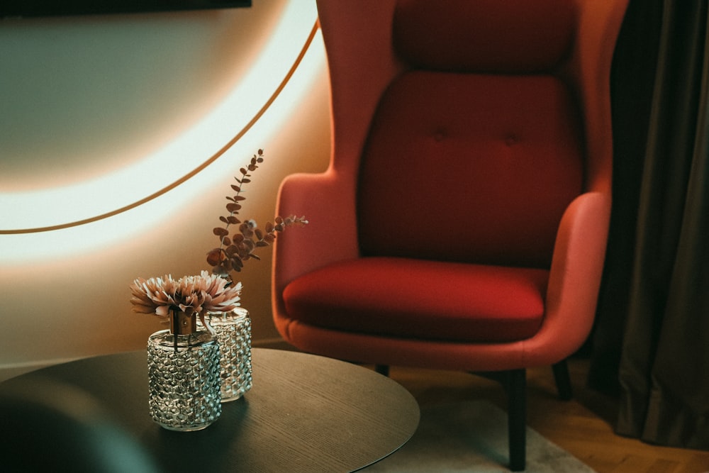 a red chair sitting next to a table with a vase of flowers