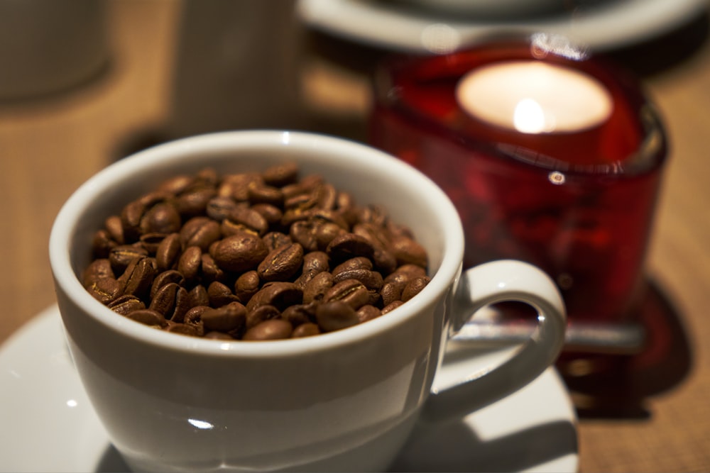 a white cup filled with coffee beans on top of a white plate