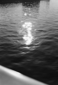 Light reflections shimmer on the surface of calm water, creating a path of bright spots leading into the distance. The image has a serene and tranquil quality, with gentle ripples visible across the water.