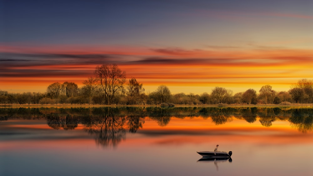 a small boat floating on top of a lake under a colorful sky