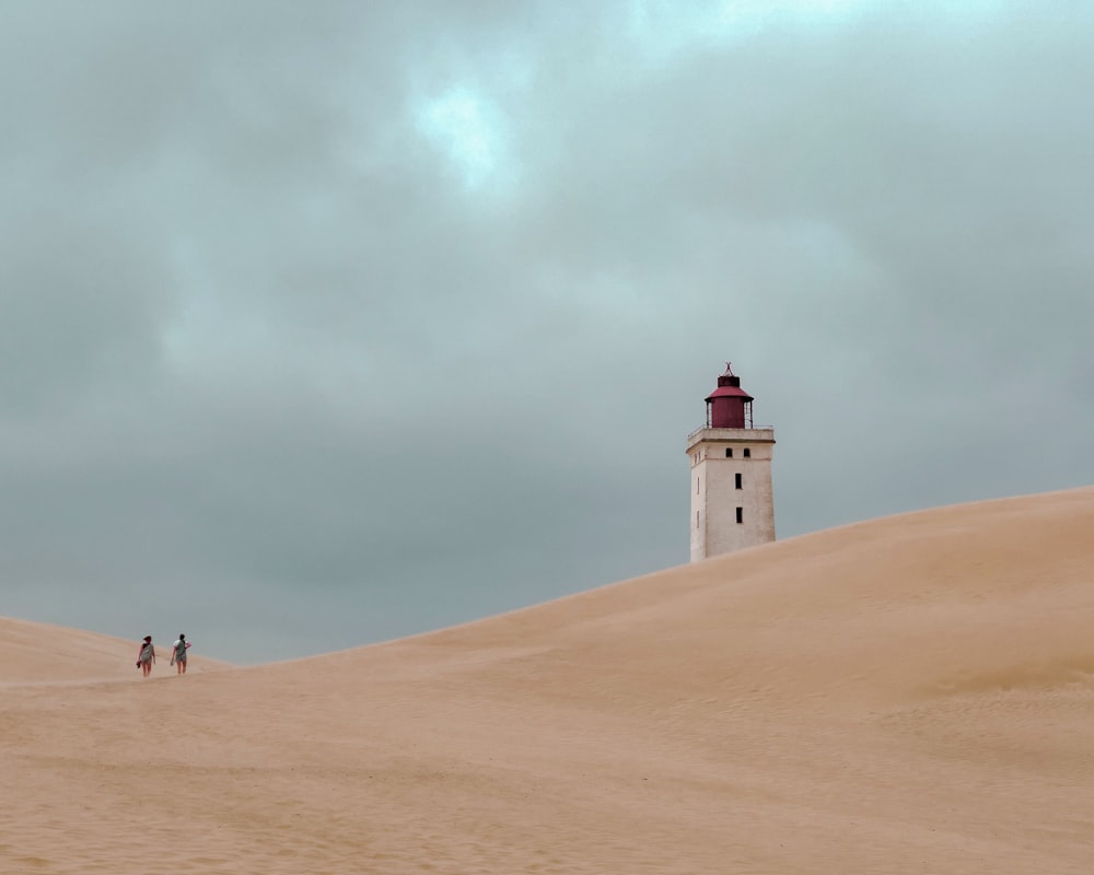 three people walking up a sand dune towards a light house