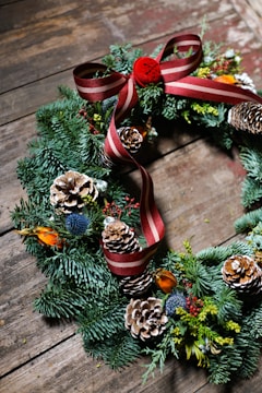 a christmas wreath with pine cones and red ribbon