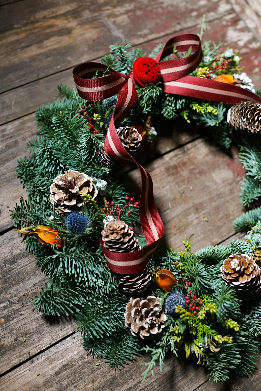 a christmas wreath with pine cones and red ribbon