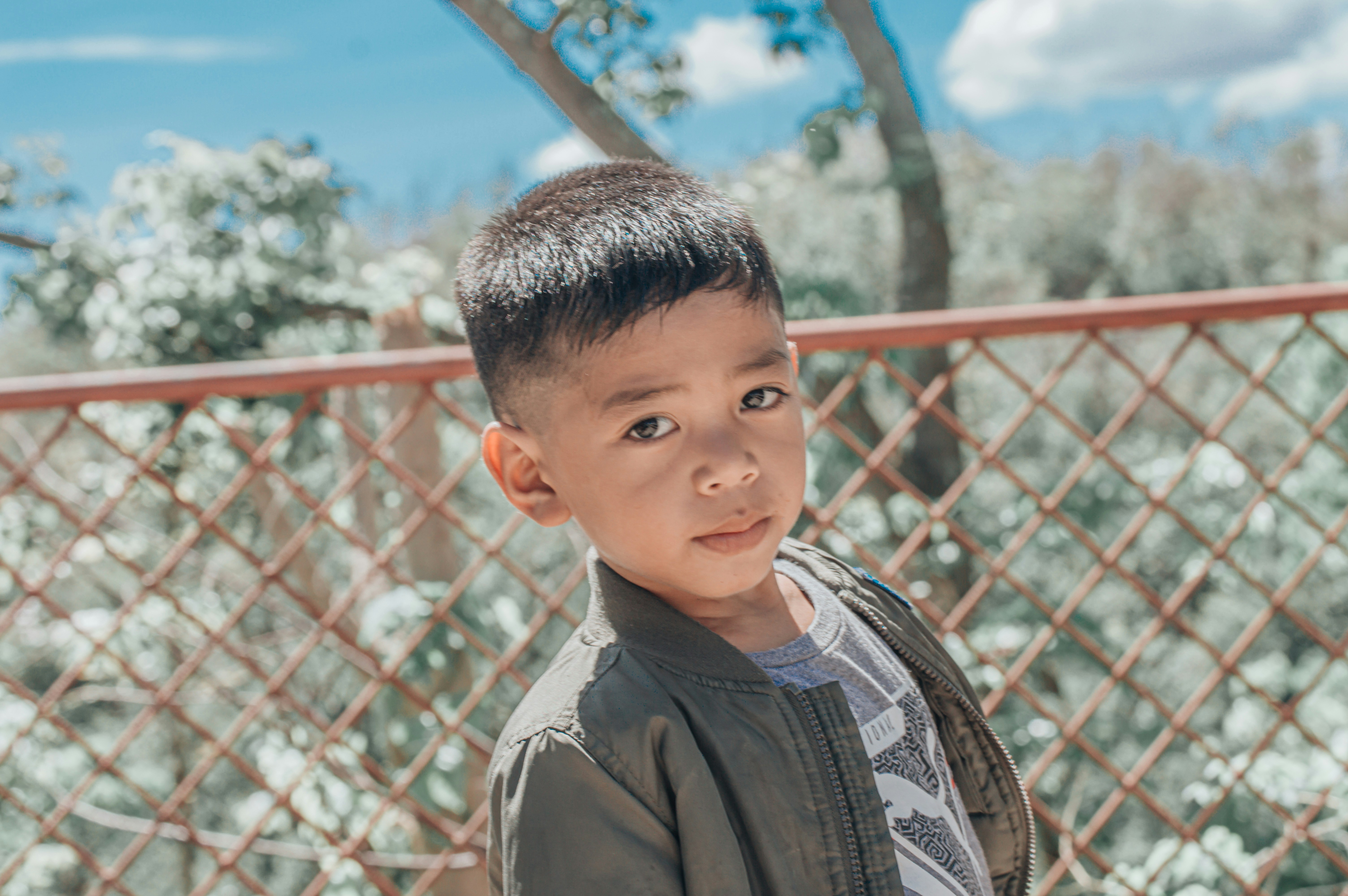 a young boy standing in front of a fence